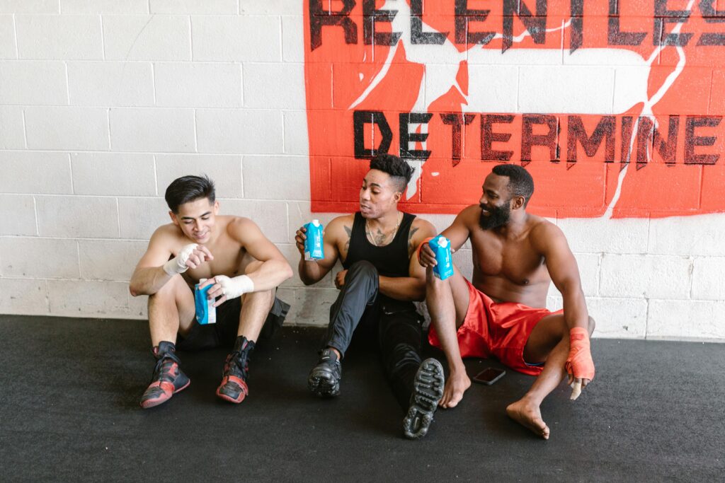 Three men sitting on the floor, displaying a sign that reads "relentless determination" after an intense workout session.