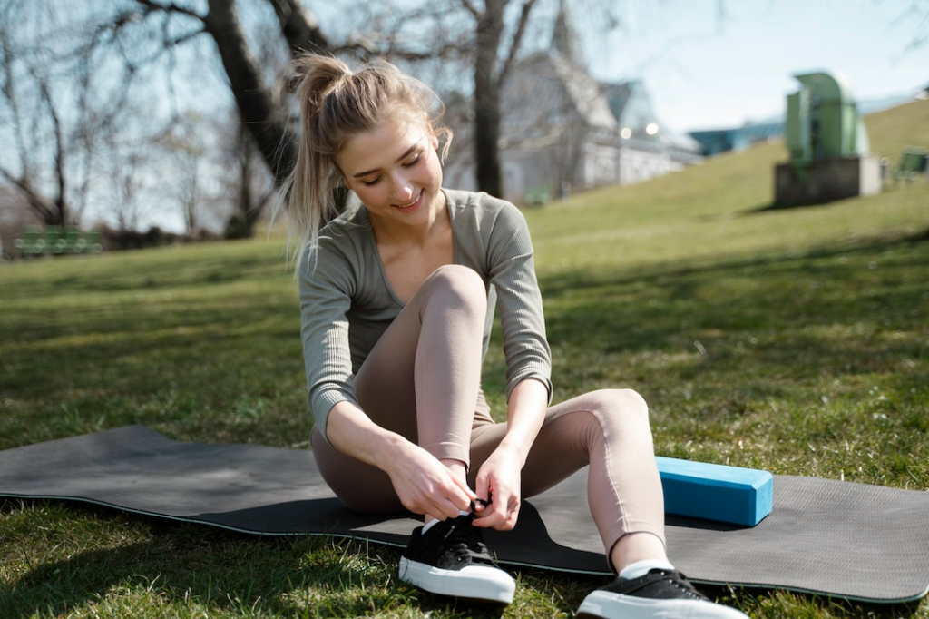  A woman sits on a mat, tying her shoes, preparing for heel pad exercises to prevent injury and improve foot health.
