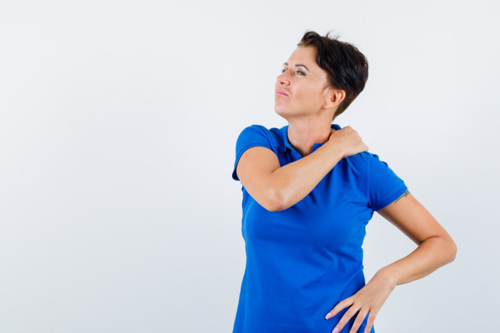 A woman with shoulder bursitis holds her shoulder, gazing directly at the camera with a concerned expression.