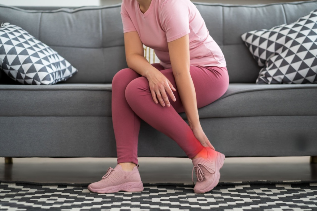 A woman sits on a couch, her foot resting on the floor, illustrating symptoms of plantar fasciitis.