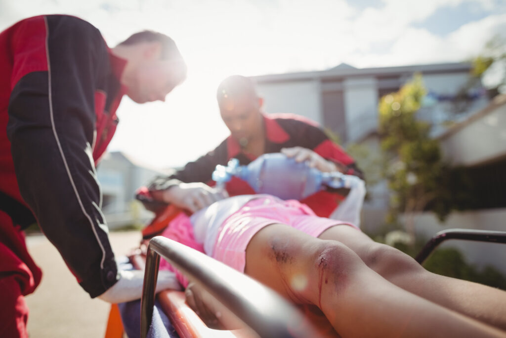 A man in red attire carries a woman on a stretcher, symbolizing support during her recovery from injury.