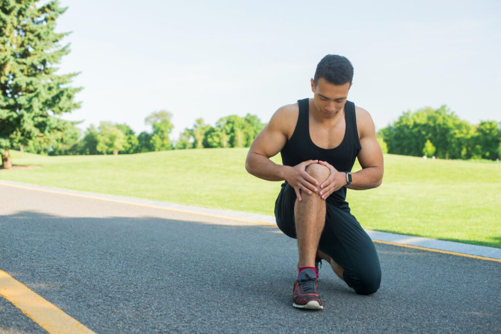 A man kneels on the road, grimacing in pain, highlighting the need for concern about his knee injury.
