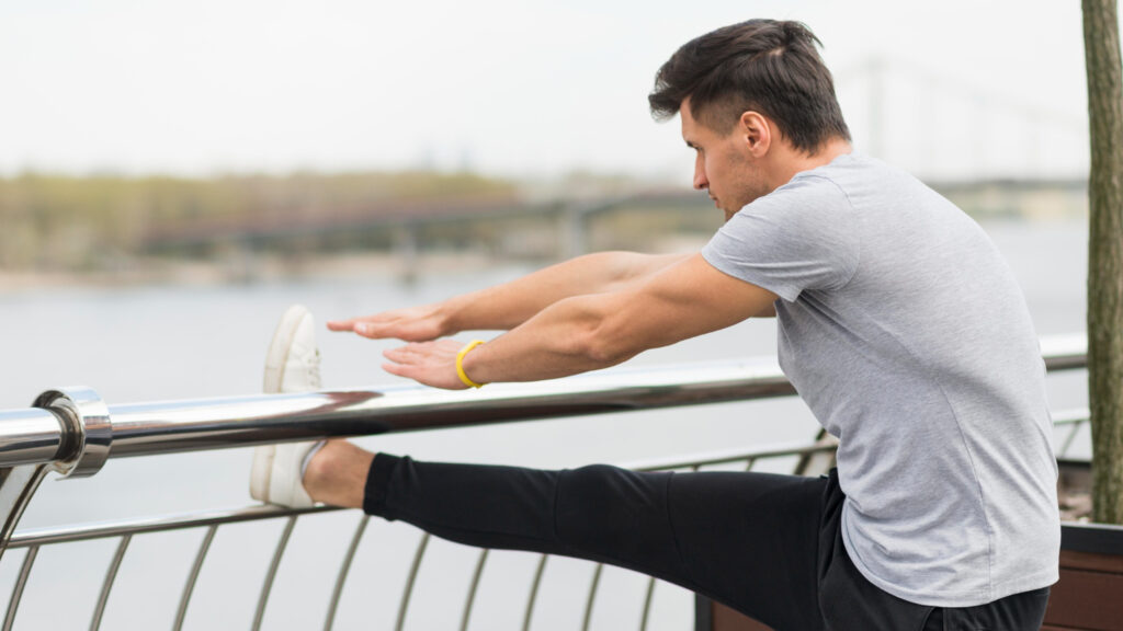 A man stretches on a railing, demonstrating techniques for enhancing muscle flexibility and overall physical health.
