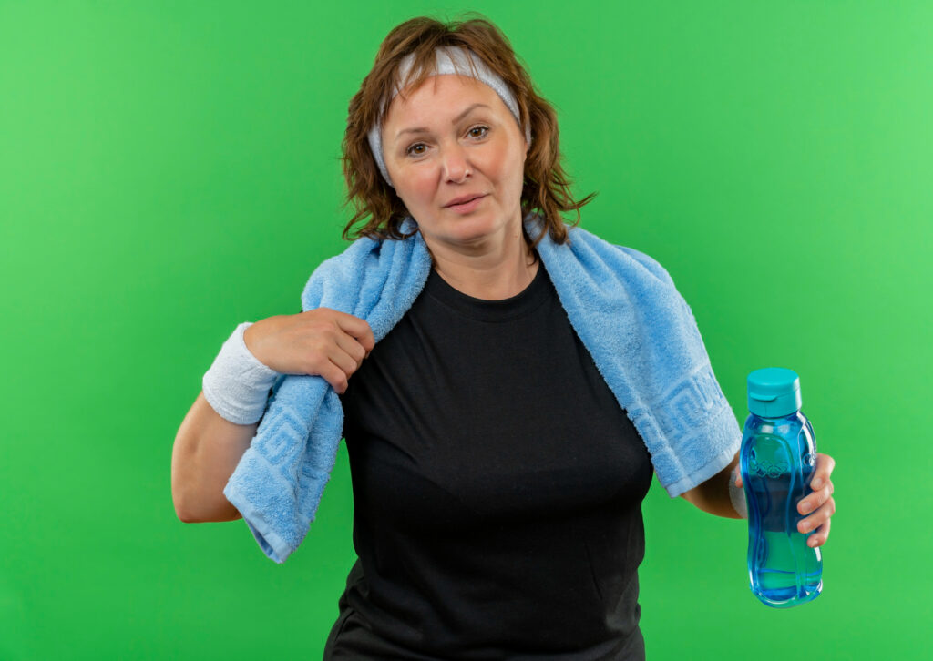 A woman holds a towel and a water bottle, ready to tackle her fitness challenges with determination and focus.