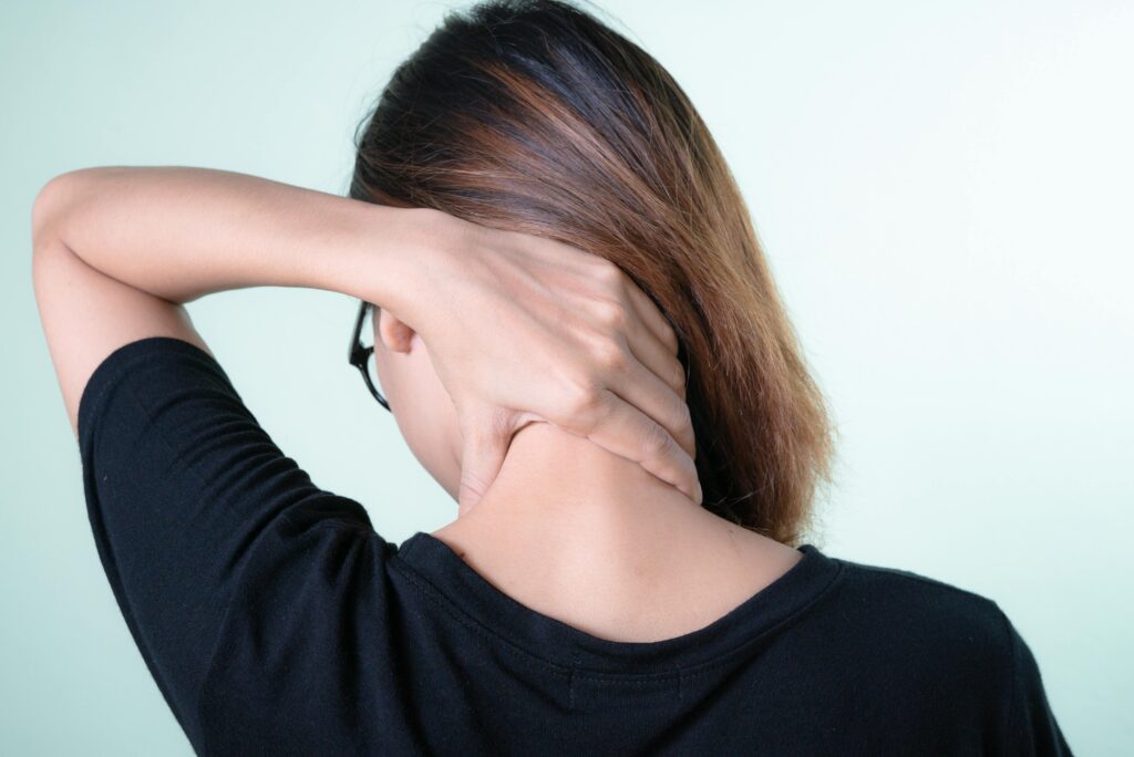 A woman gently stretches her neck, practicing at-home exercises for relaxation and maintenance of her well-being.