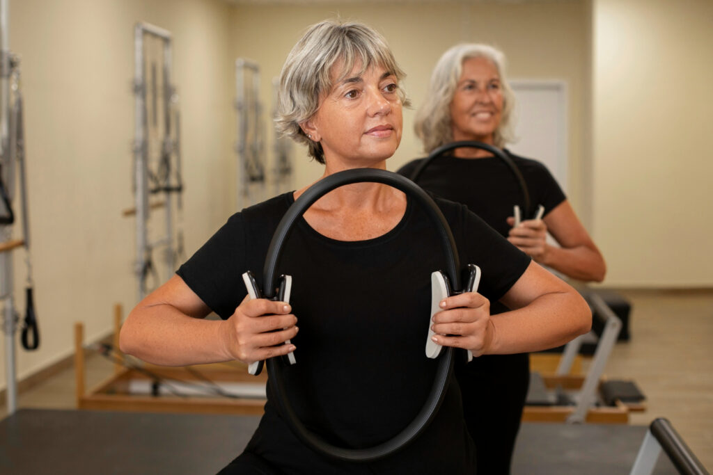 Two women engaged in a pilates class, using hoops, fostering a supportive and encouraging atmosphere together.