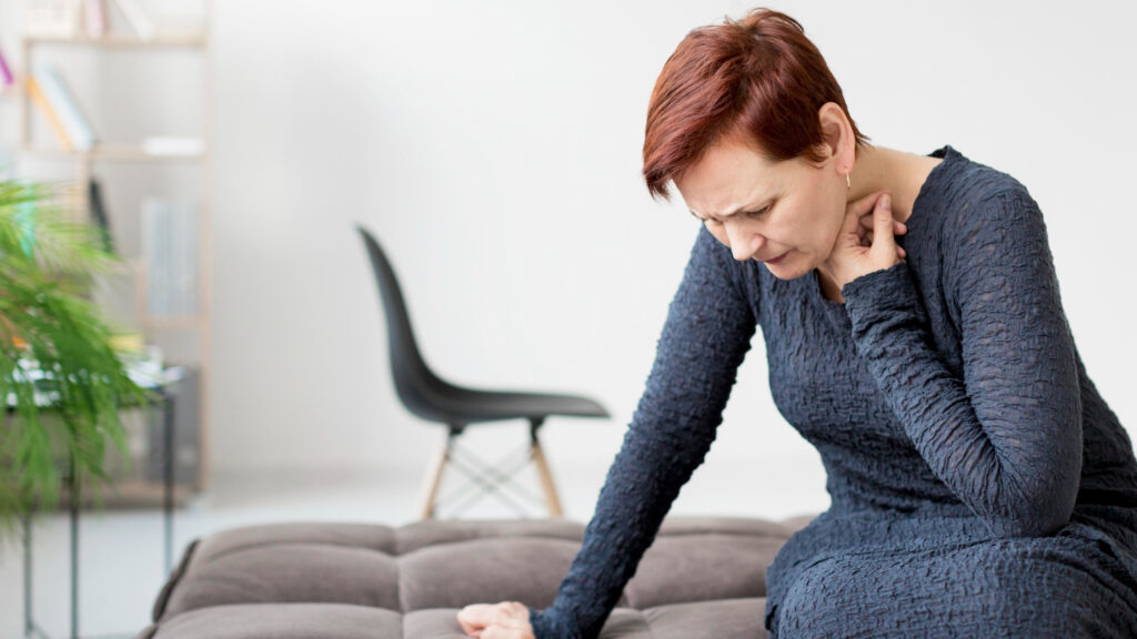 A woman sits on a couch, gently massaging her neck, possibly due to rib pain from persistent coughing.