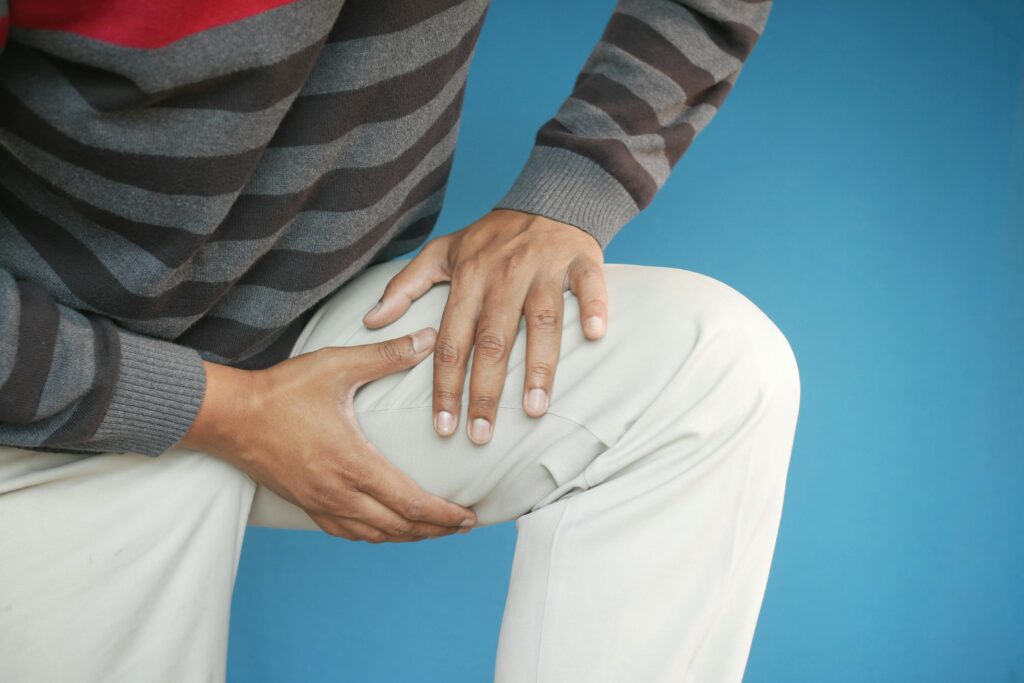 A man grimaces in pain, holding his knee, highlighting the discomfort caused by tight muscles and knee issues.