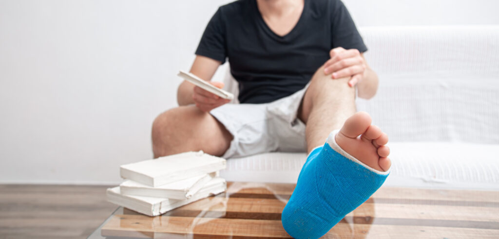 Man sitting on a couch with a blue cast on his foot, holding a book. Learn how to heal a sprained foot overnight with effective recovery methods.