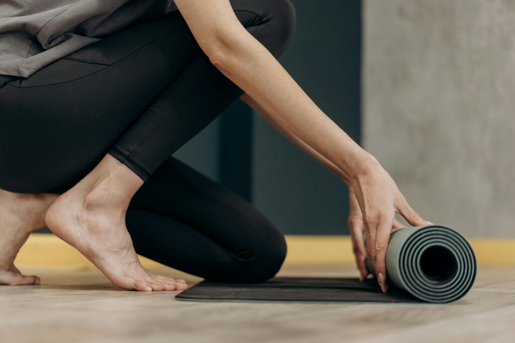 A woman lays a yoga mat on the floor, preparing for a self-care session focused on relieving muscle knots.