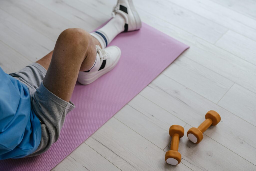 A person on a mat holds two dumbbells, focusing on rehabilitation and strength training techniques.
