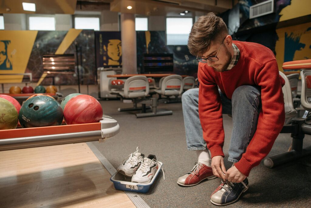 A man kneels to tie his shoes at a bowling alley, preparing to return to the fun of the game.