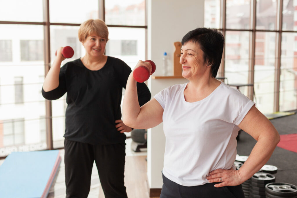 Two women lifting weights in a gym, focused on setting realistic and sustainable fitness goals together.