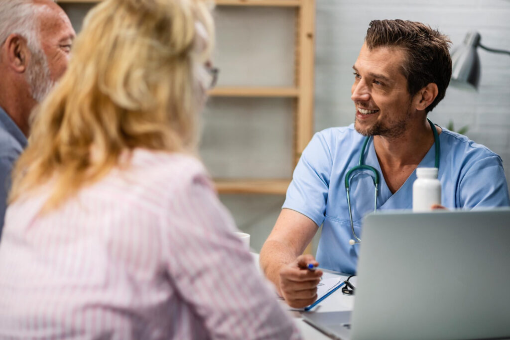 A man in blue scrubs converses with a woman and another man, showcasing a collaborative healthcare environment.
