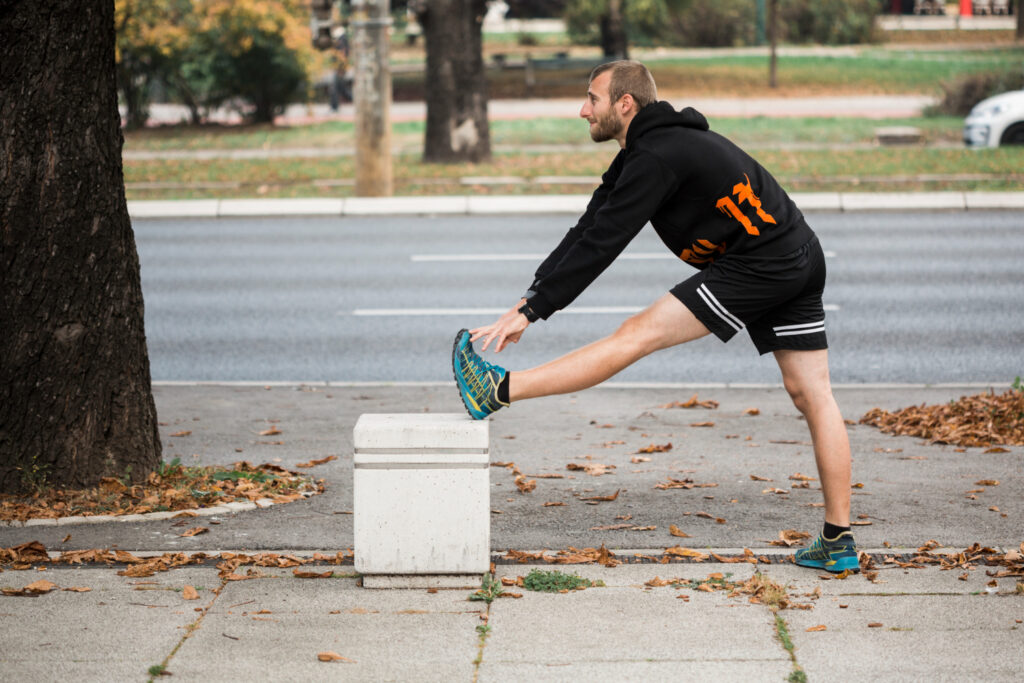 A man performing a stretch on a street corner, demonstrating techniques for hamstring, quadriceps, and calf stretches.