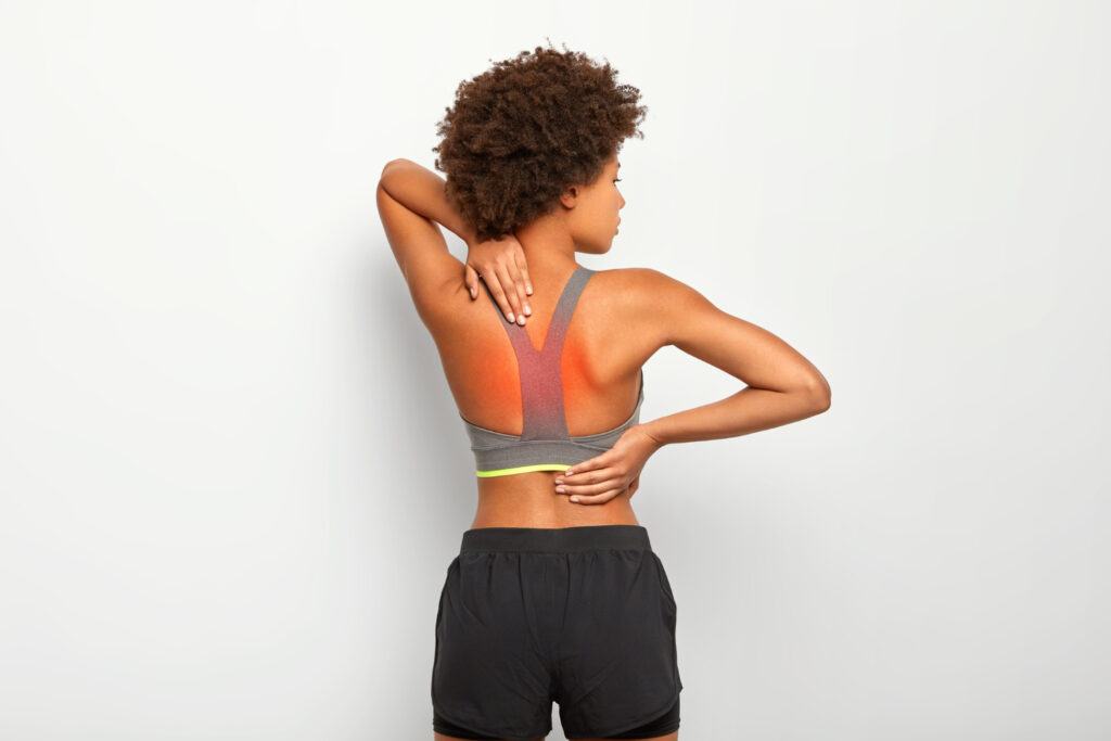 Woman with back pain, holding her shoulder, illustrating symptoms of back muscle knots and discomfort.