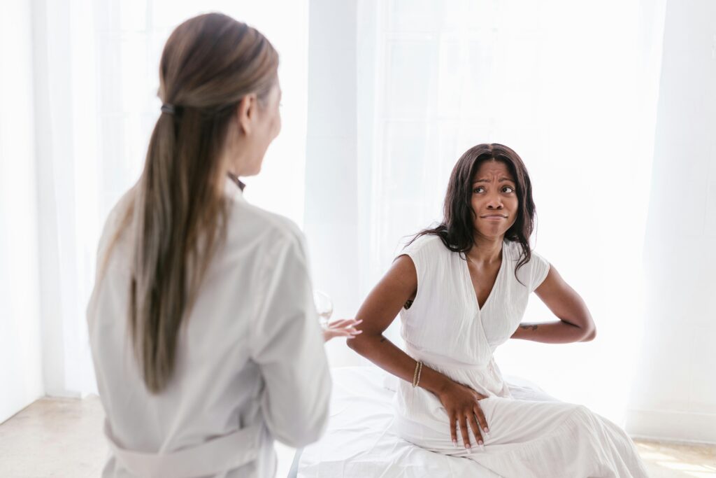 A woman discusses her symptoms with a doctor while sitting on a bed, focusing on buttocks trigger points.