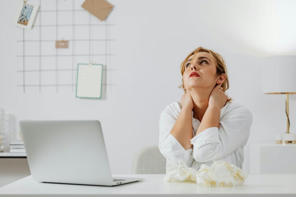  A woman at her desk, gently massaging her neck, reflecting on the impact of lifestyle factors on well-being.