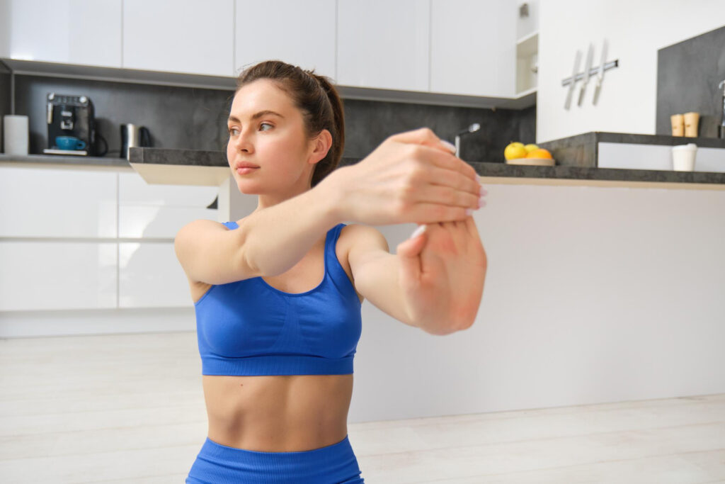 A woman in a blue sports bra and shorts performs a stretching exercise, focusing on wrist flexibility and strength.