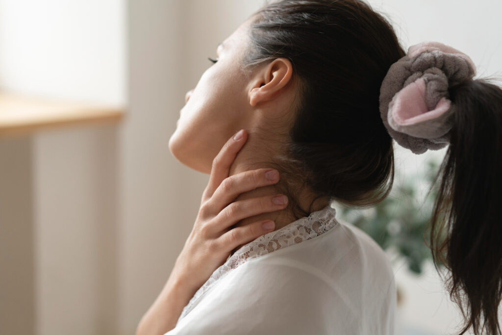 A woman touching her neck in discomfort, showing signs of stiffness, illustrating how to unlock wry neck with proper techniques for pain relief.