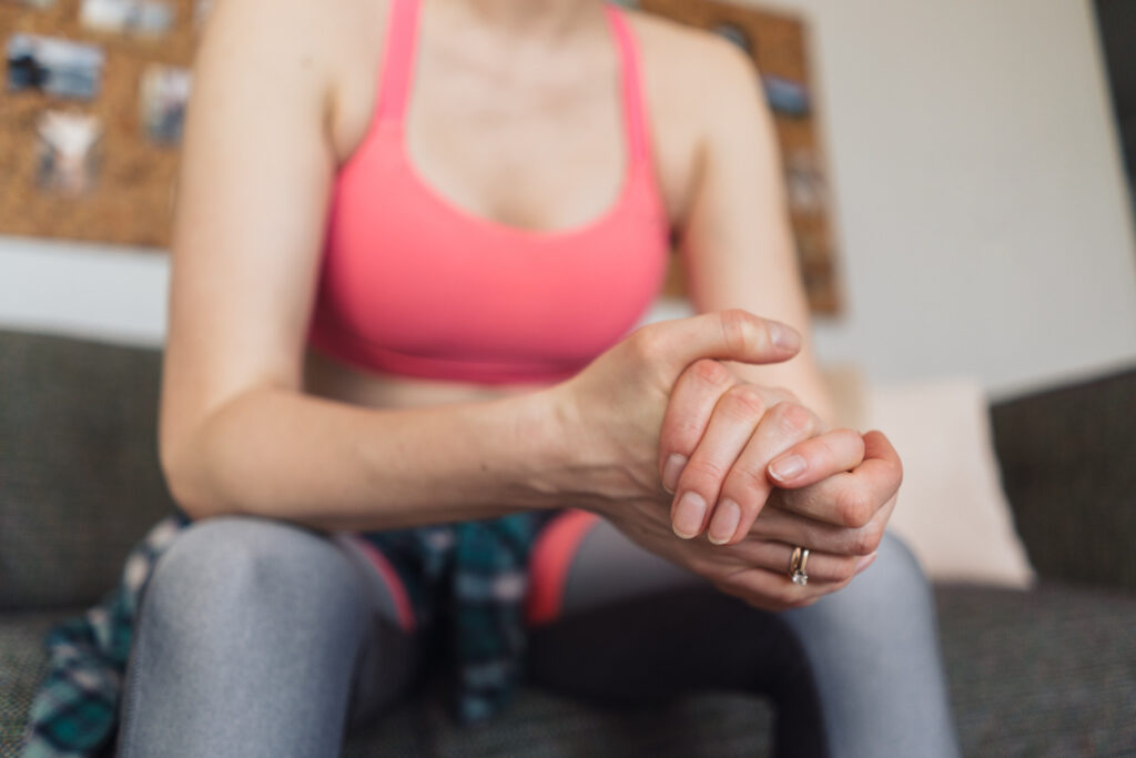 A woman sitting on a couch in workout attire, holding her wrist and performing an exercise, demonstrating how to strengthen your wrists effectively.